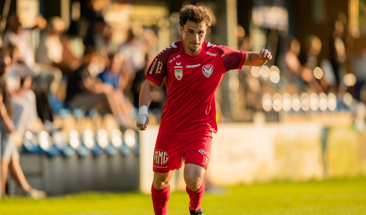 Fußballspieler im roten Trikot mit Bandage am Arm spielt auf einem Rasenplatz